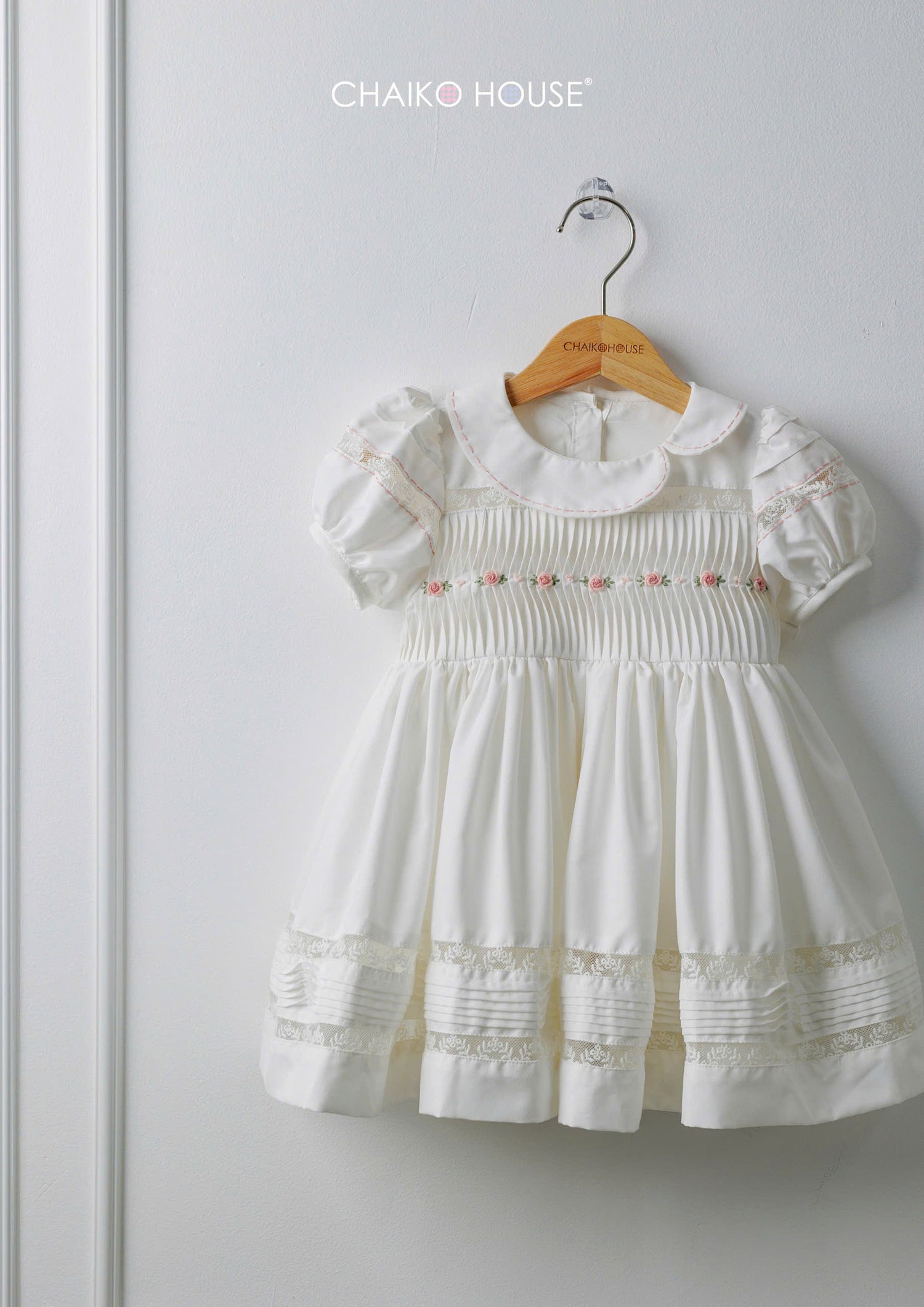White baby girl dress with pintuck bodice and lace hem on hanger