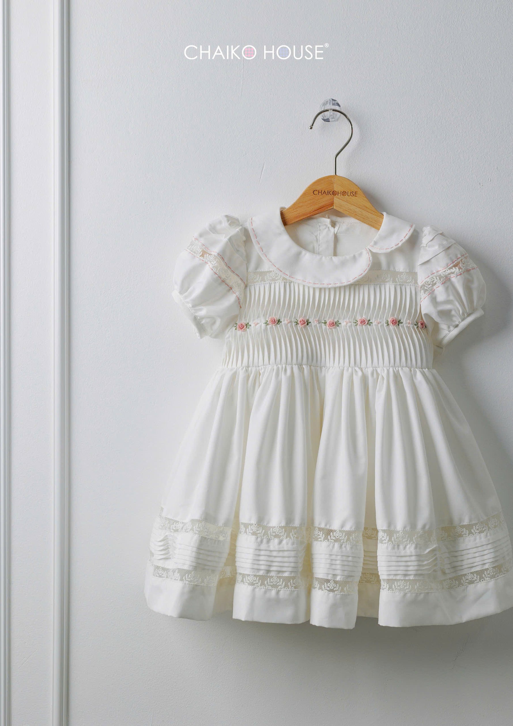 White baby girl dress with pintuck bodice and lace hem on hanger